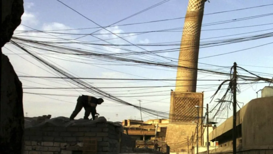 Na archívnej snímke elektrotechnik pracuje na streche obchodu v meste Mósul v severnom Iraku. V pozadí je naklonený minaret mešity al-Núri.