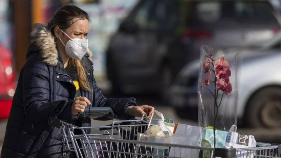 Na snímke žena s respirátorom vychádza z potravín